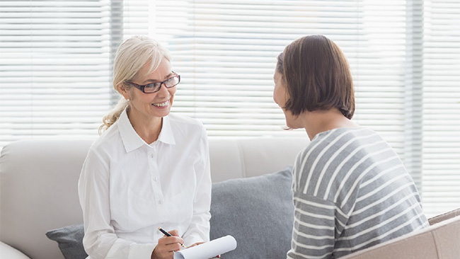 A therapist in a white blouse meets with a client in a striped shirt, both are smiling