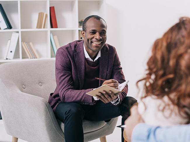 A provider sits in a well-lit room, taking notes as he meets with a client