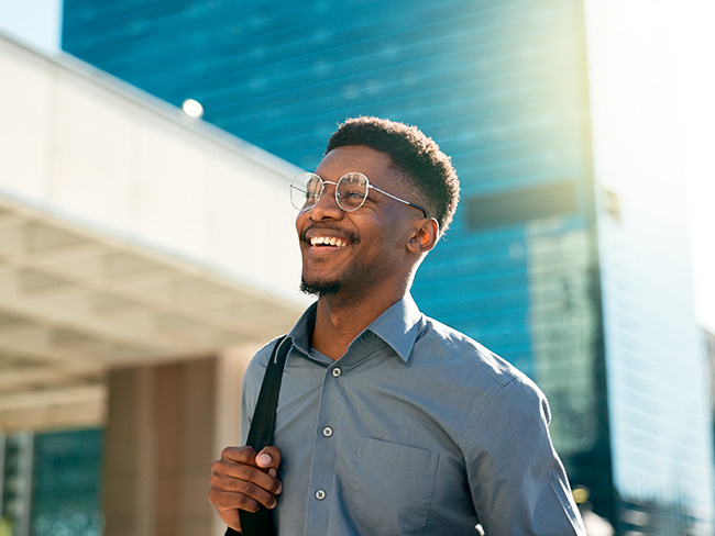 A young man strolls down the street on a bright sunny day, wearing a backpack and business casual clothing