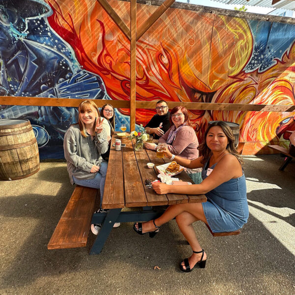 Mindful Support Services staff celebrate outside on the patio of a brewery, a large colorful mural in the background