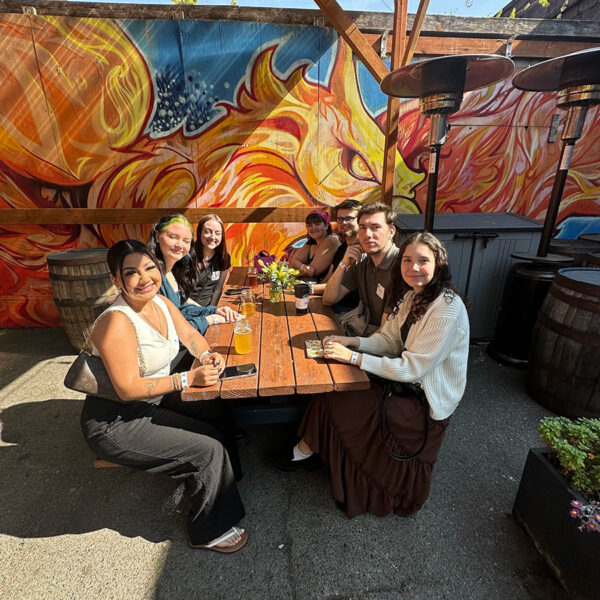 Mindful Support Services staff celebrate on the patio of a brewery, a large colorful mural in the background
