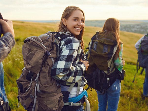 A young woman looks back over her shoulder and smiles while backpacking through a meadow with friends