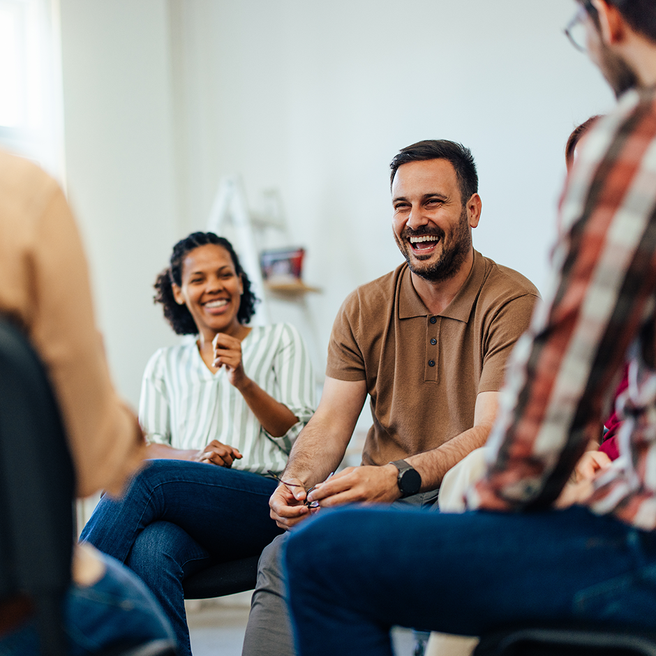 An adult man, looking happy, talking with random people from the group therapy.
