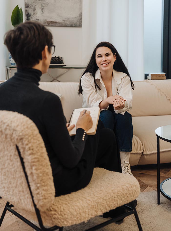 Psychologist writing down notes during therapy session with smiling woman