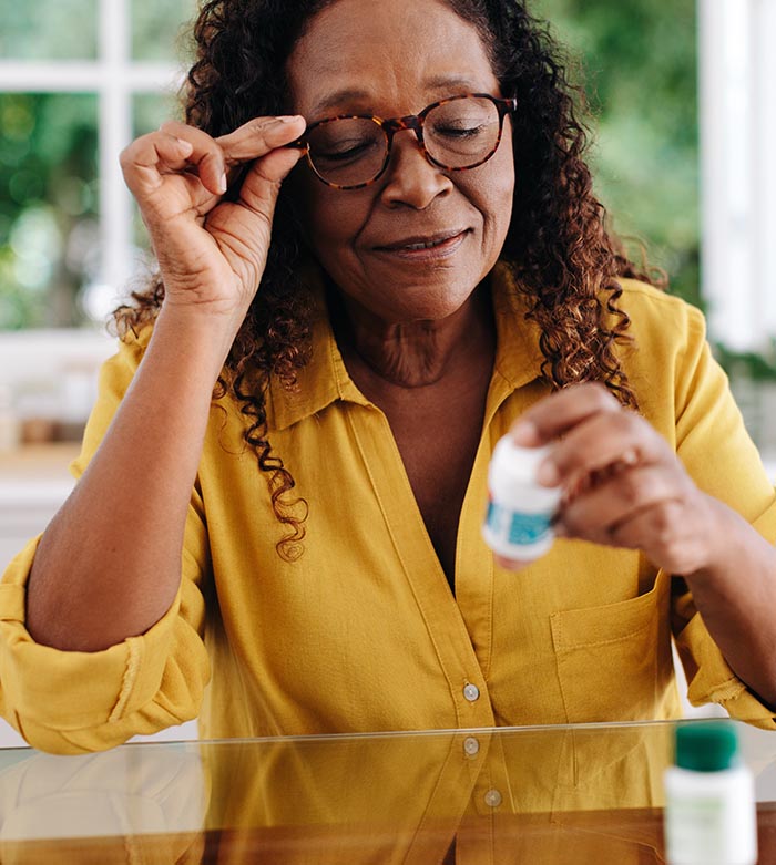 A woman in a yellow shirt holds a pill while reading a prescription bottle