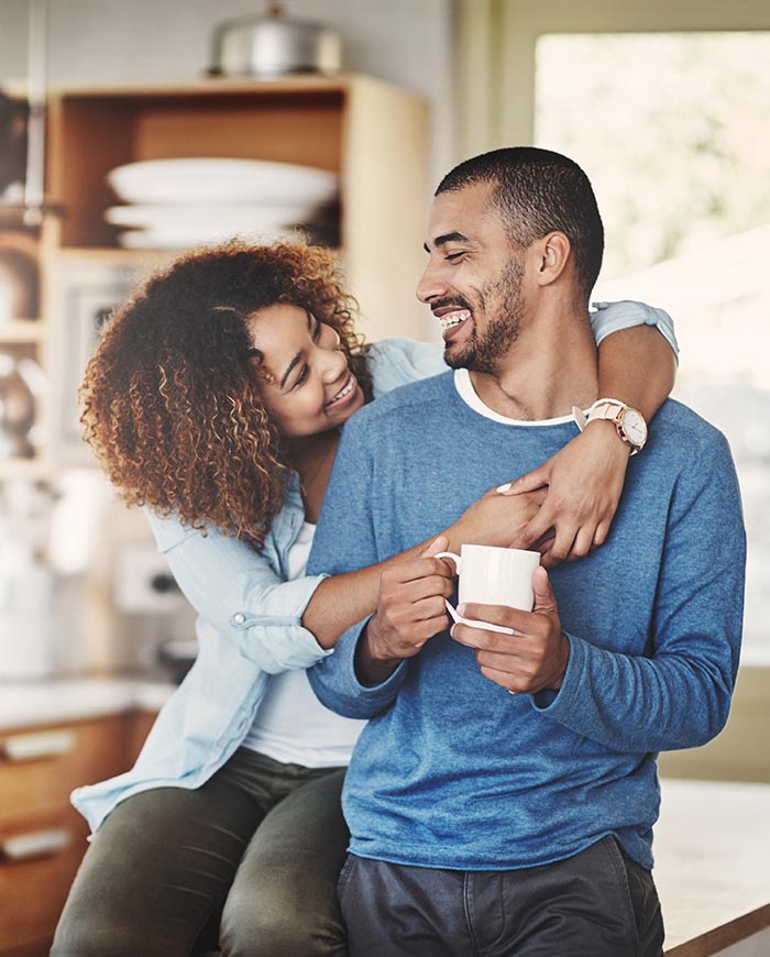 Happy couple hugs while having coffee in kitchen.
