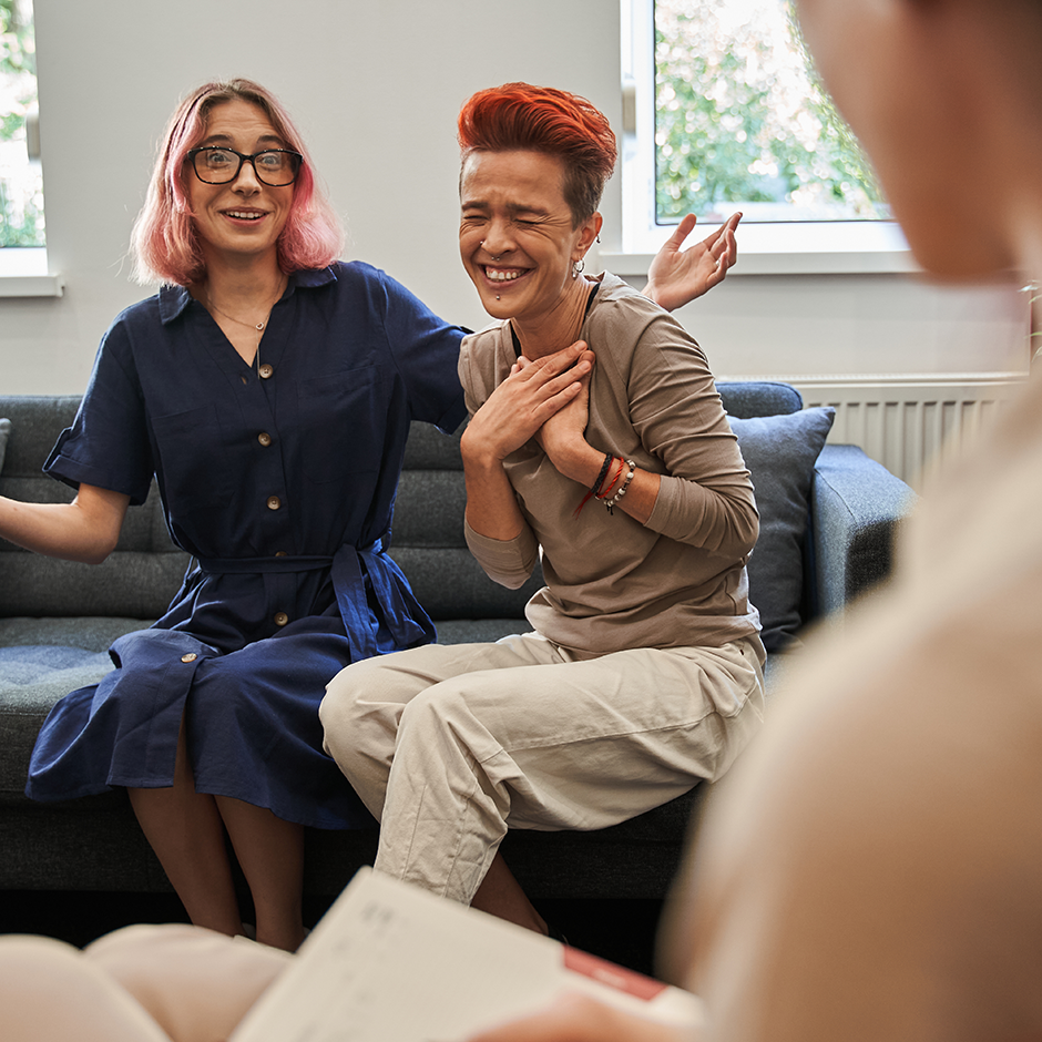 Lesbian married couple laughing out loud while talking and sitting on the therapy session