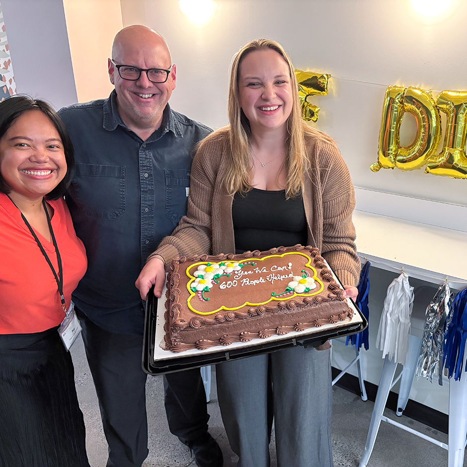 Three people standing with cake celebrating 600 intakes in one day with a 